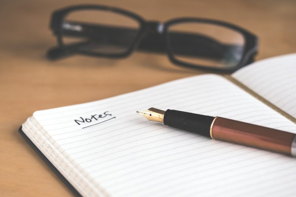 明るい机の上でノートに未来の予定や目標を書くイメージ。Photo by Jess Bailey on Unsplash