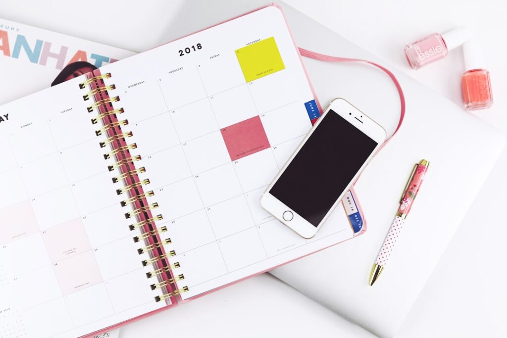 明るいデスクで手帳とスマートフォンを使って予定を整理するイメージ。Photo by Hey Beauti Magazine on Unsplash